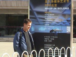 Artist, Craig Walsh outside the China Millennium Monument Art Museum, Beijing standing with the exhibition's poster featuring his art work. 22 October 2002.